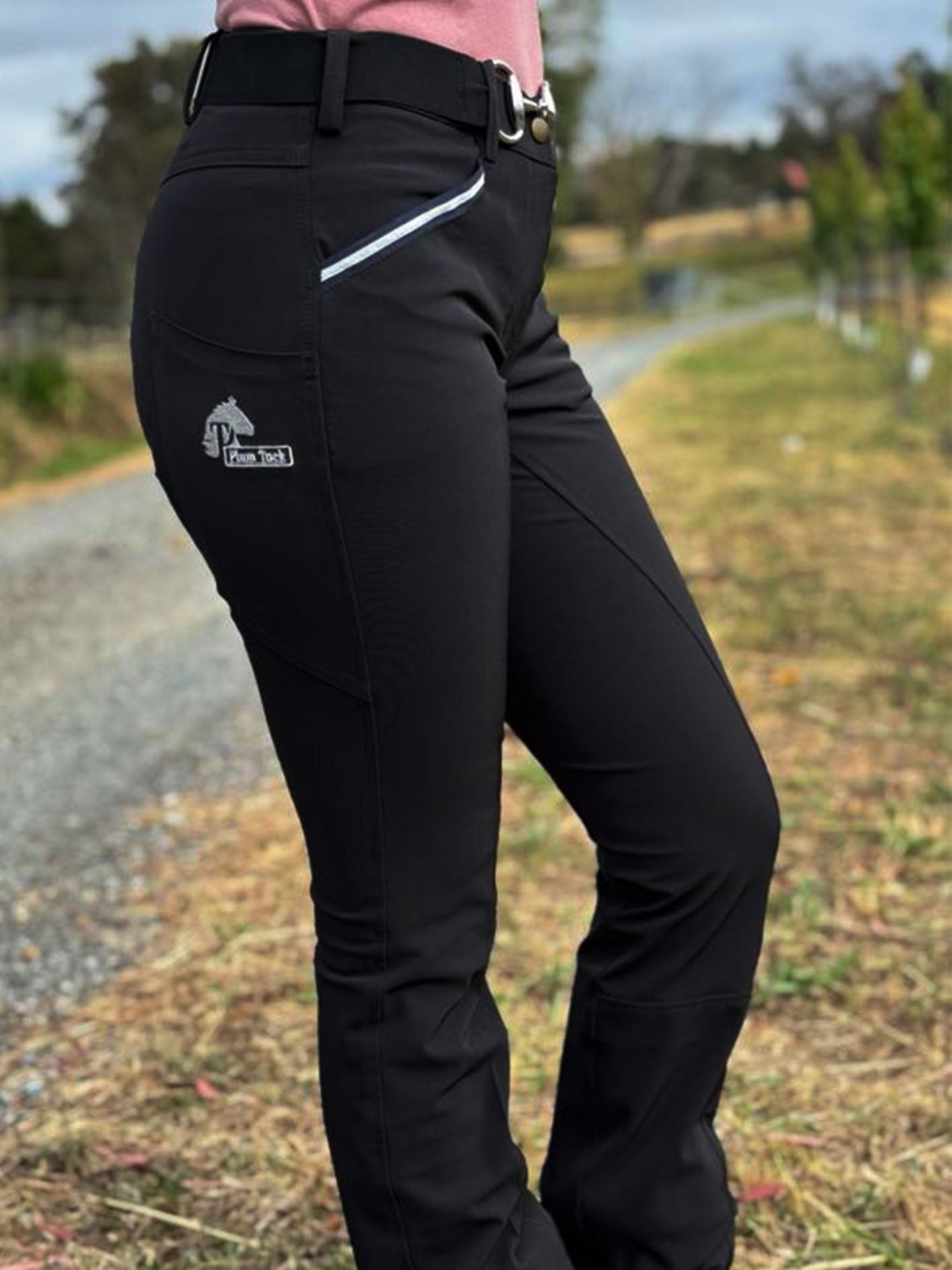 Shows woman wearing the bootleg riding pants. Also shows the phone pocket and logo.