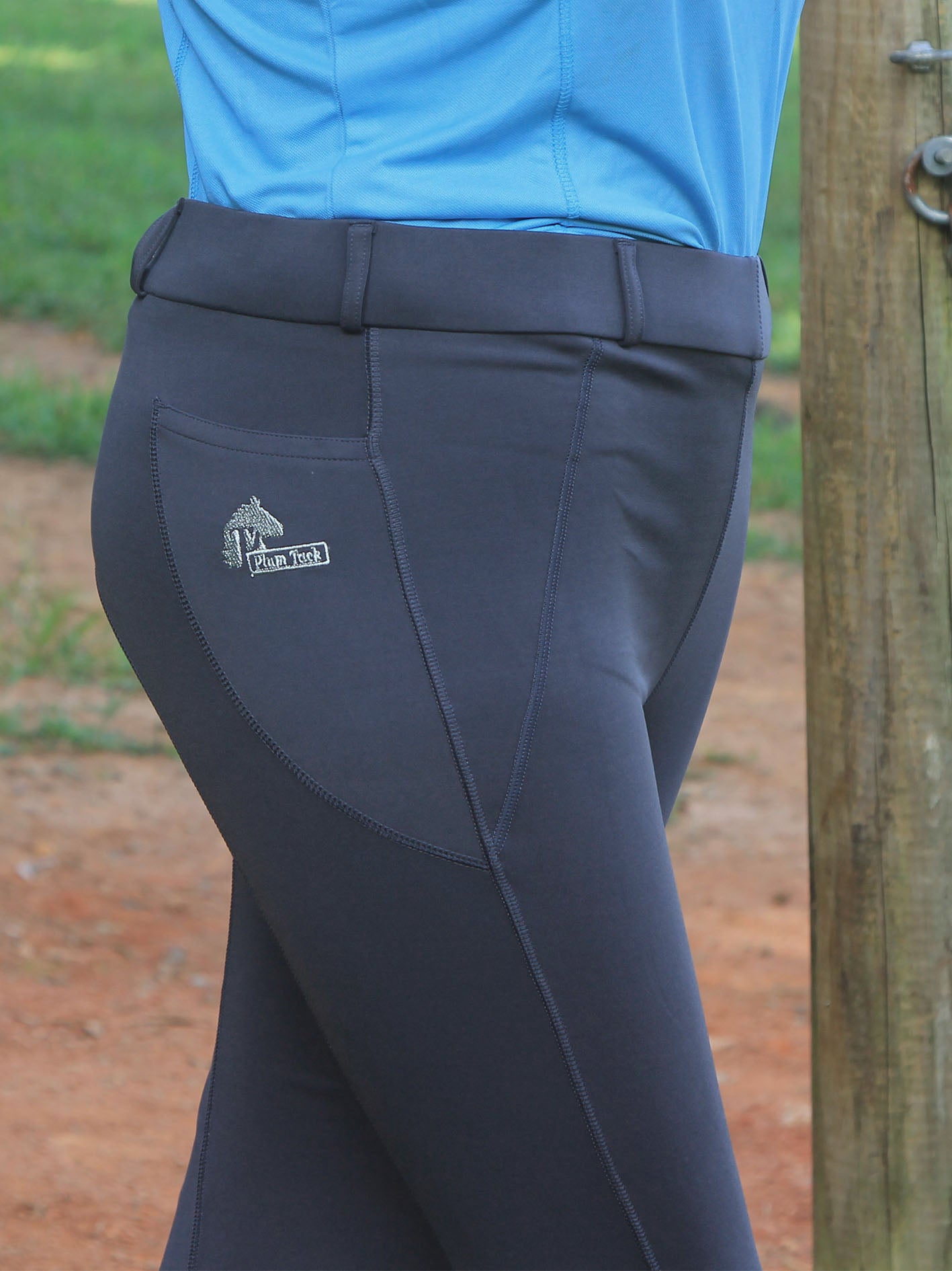 Dark gray riding pants with a logo on the pocket, worn by a person in a blue shirt.