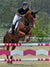 Woman show jumping wearing navy and white show shirt